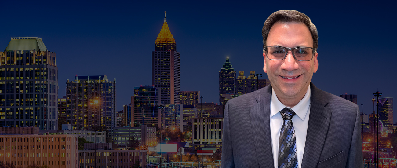 Photo of Glenn T. Stern in a business suit smiling in front of an illuminated city skyline at dusk.